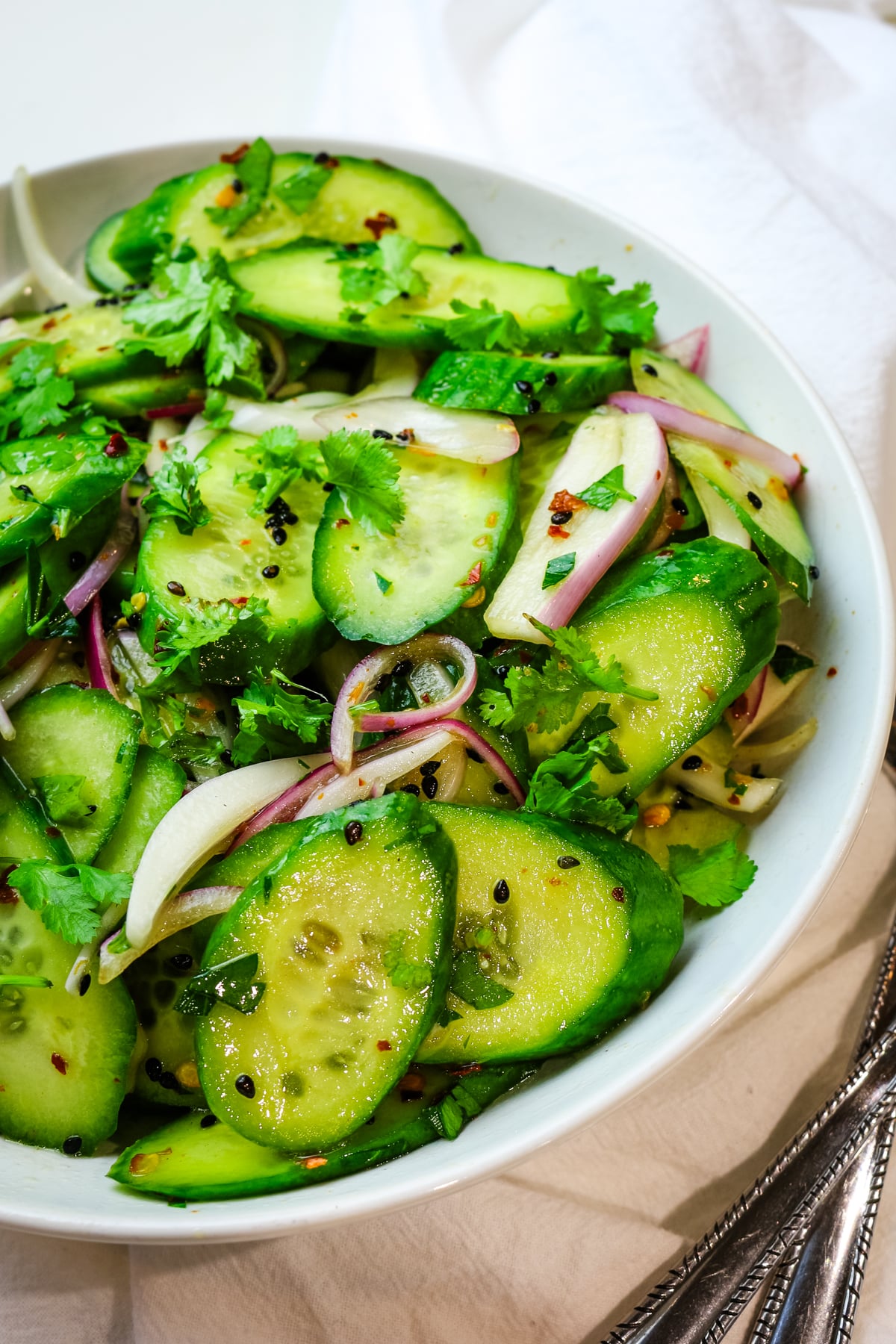 close up of cucumber salad with red onions, cilantro, and black sesame seeds.