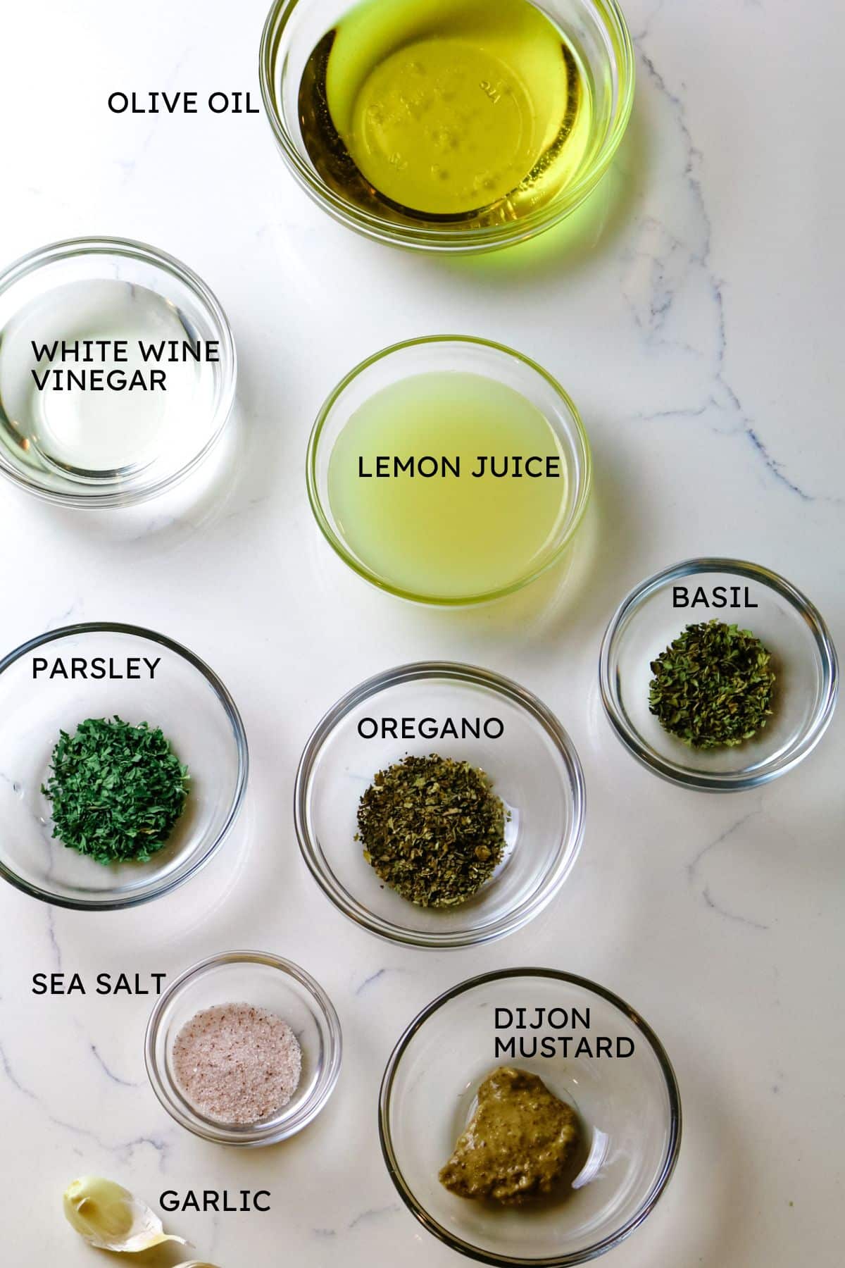 ingredients for salad dressing with olive oil, white wine vinegar, lemon juice, herbs, and Dijon mustard.