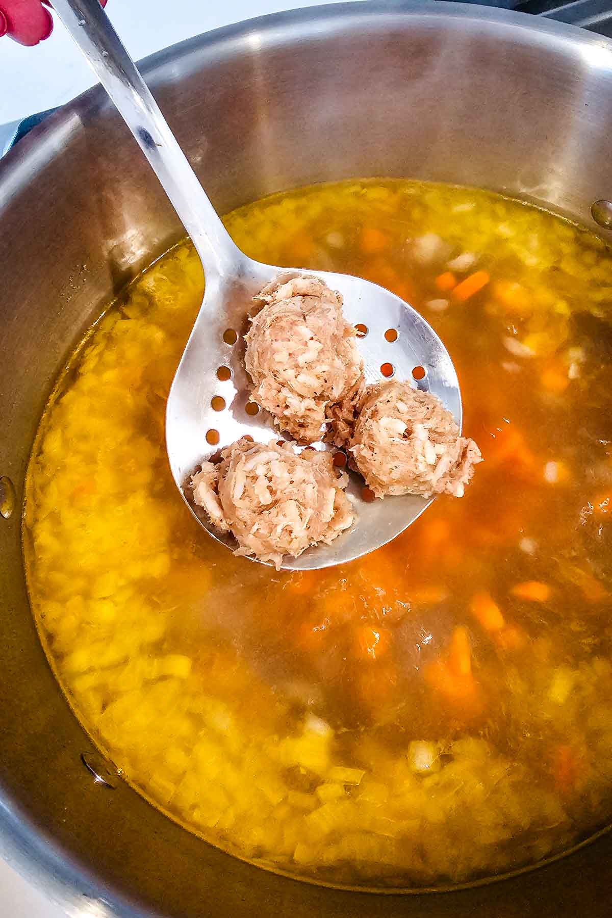 meatballs being added to a hot broth with veggies.