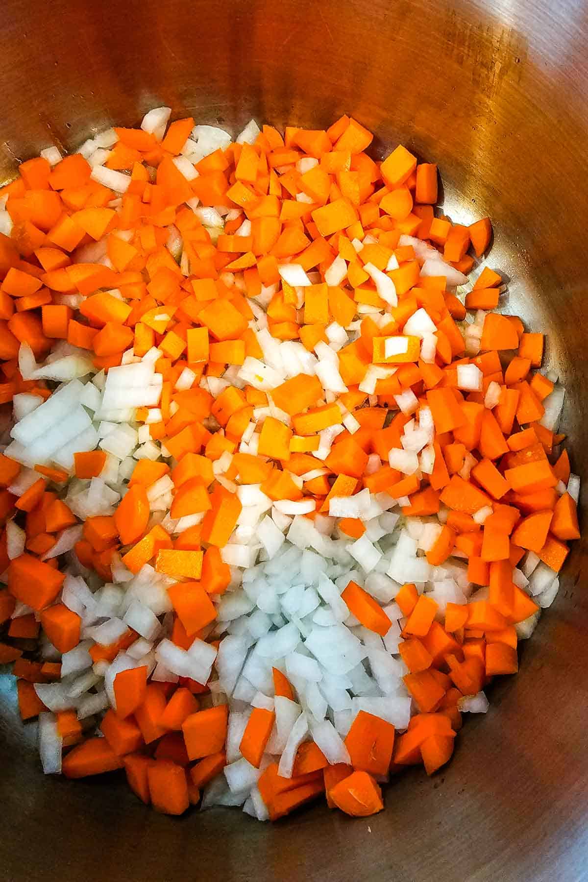 carrots and onions added to a large soup pot to be sauteed.