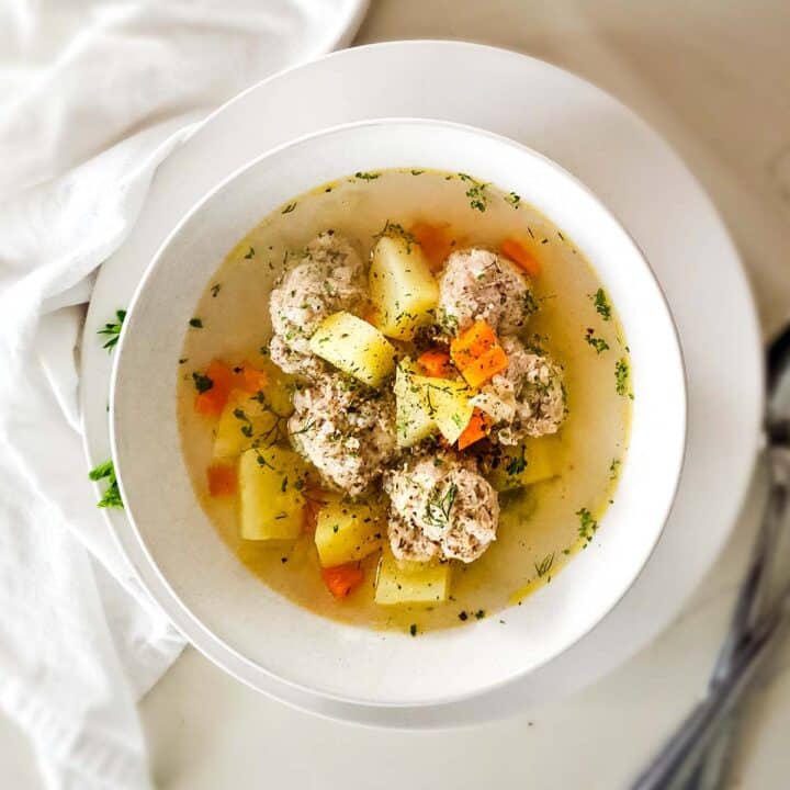 meatball soup with potatoes and carrots in a very clear broth in white bowl.