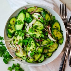 cucumber salad in white bowl with forks to the side.