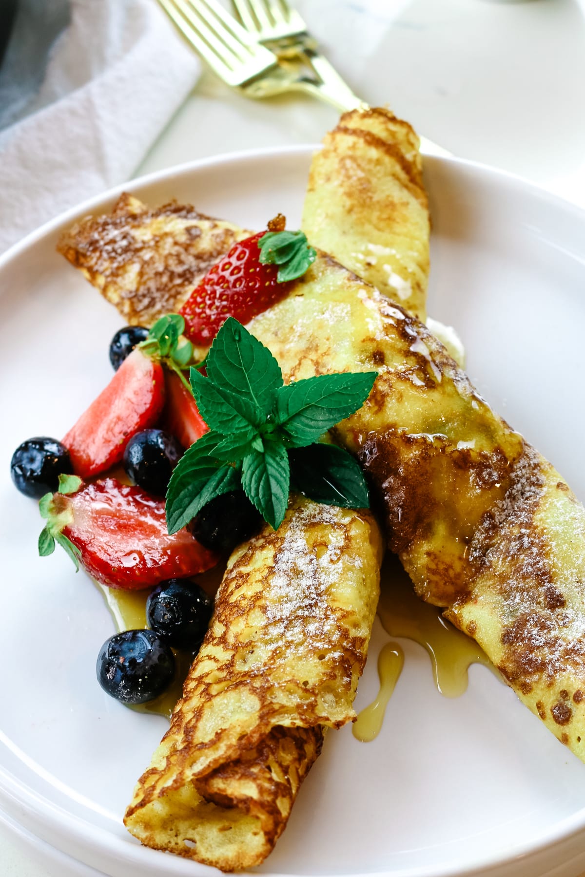 rolled up crepes on a white plate with fresh berries and fresh mint.