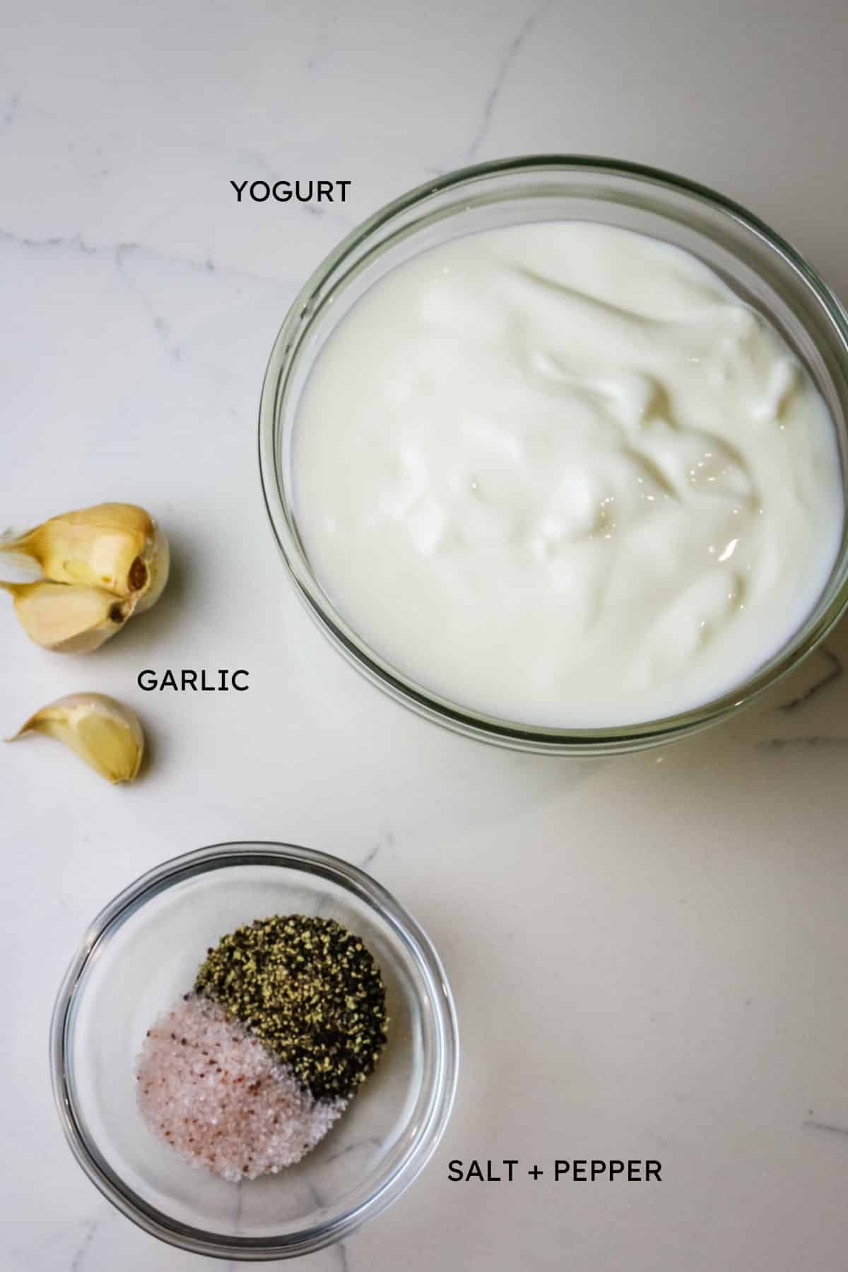 ingredients to garlic yogurt sauce on a flat white surface with labels.