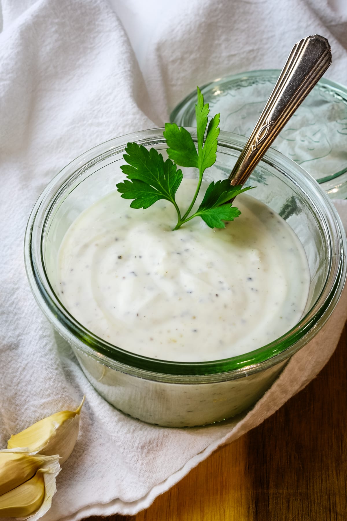 Yogurt, garlic, and black pepper in a jar with fresh flat leaf parsley sticking out.
