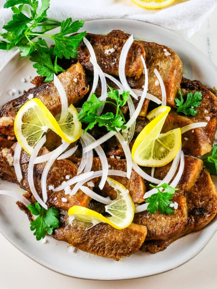 fried beef tongue with sliced white onion and lemon slices.