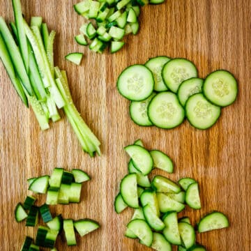 various shapes and sizes of cucumber on wooden cutting board.