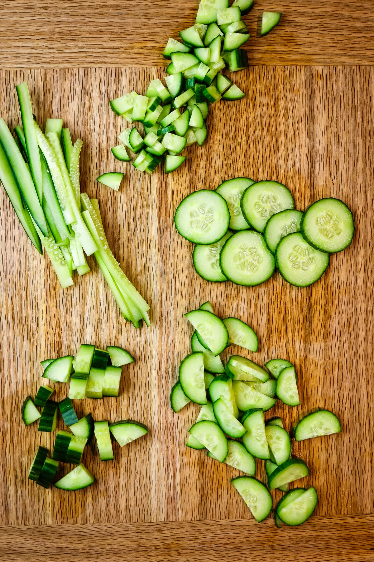 cucumber cut into various shapes and sizes on a wooden cutting board.