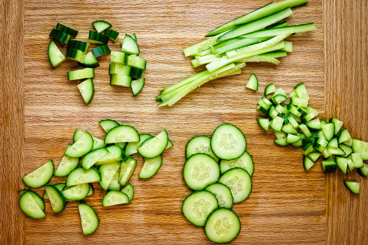 cut cucumbers in various shapes and sizes on cutting board.
