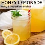 homemade lemonade in a mason jar with ice and a straw in the cup, cut lemons and pitcher of lemonade in the back.