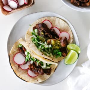 two beef tongue tacos on a platter garnished with cilantro and lime on the side.