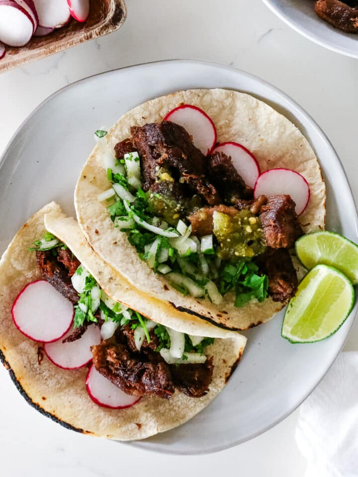 two beef tongue tacos on a platter garnished with cilantro and lime on the side.