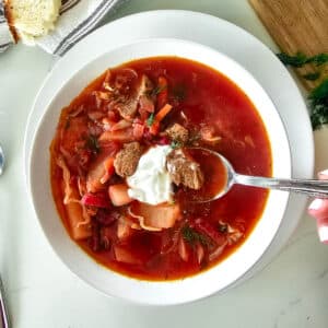 borscht in a white bowl with dollop of sour cream.