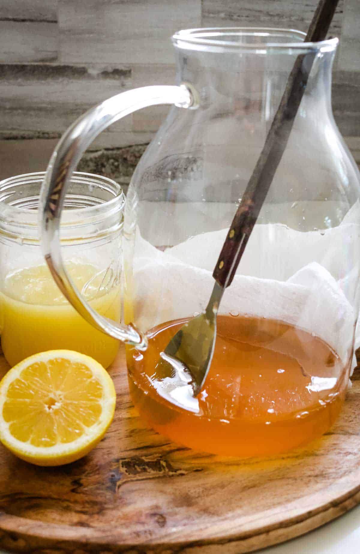 glass pitcher with honey and water stirred in with lemon juice to the side and a cut lemon half.