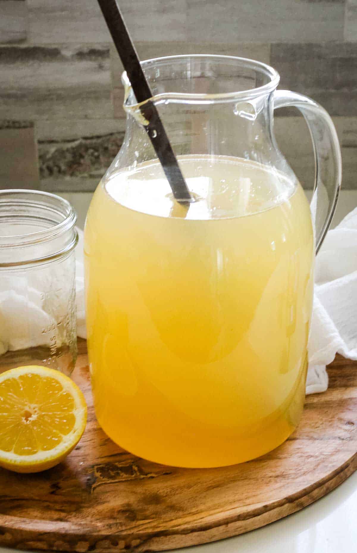 pitcher of lemonade with a long spoon sticking out and a cut lemon half to the side.