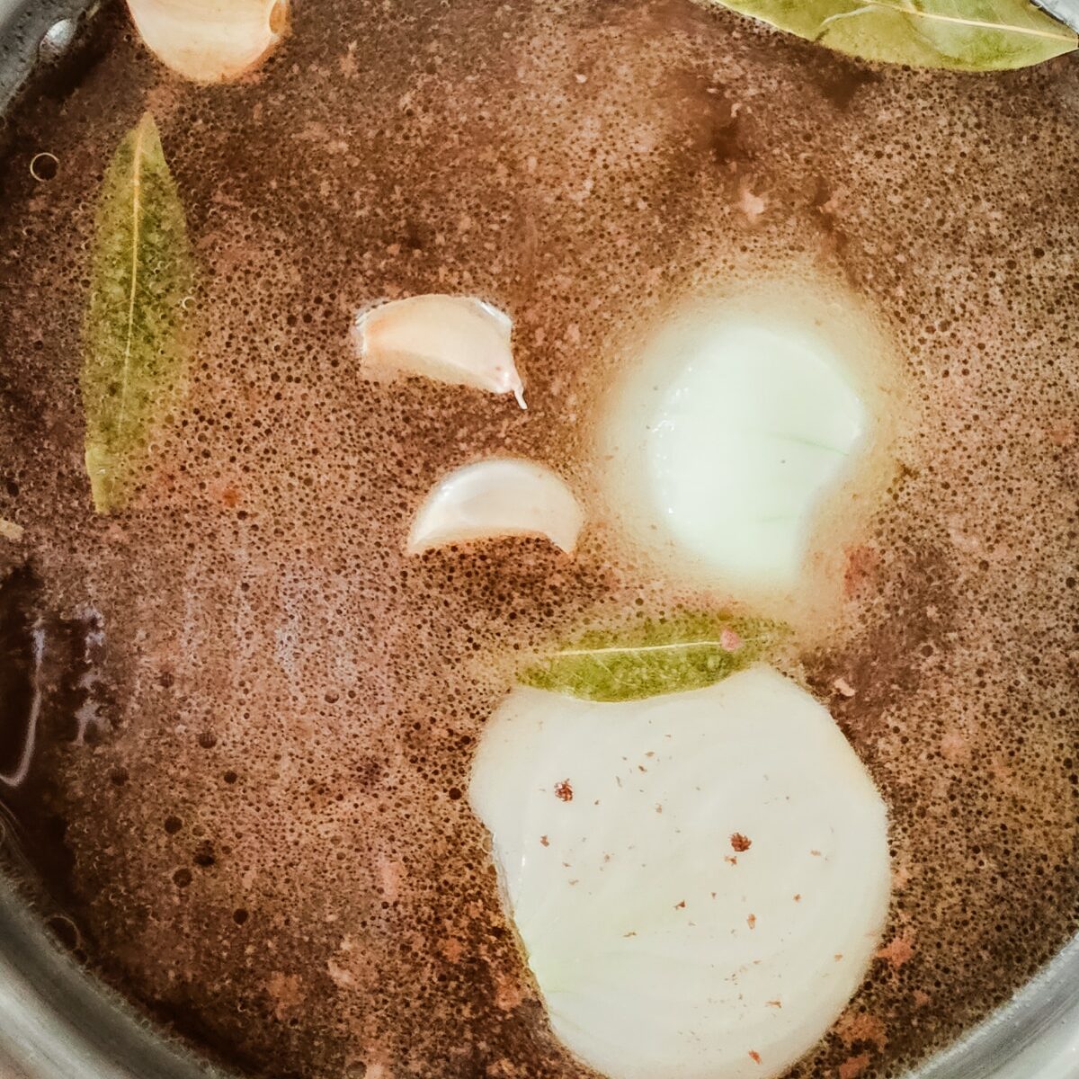 beef broth is cooked in a large pot with onions and bay leaves.