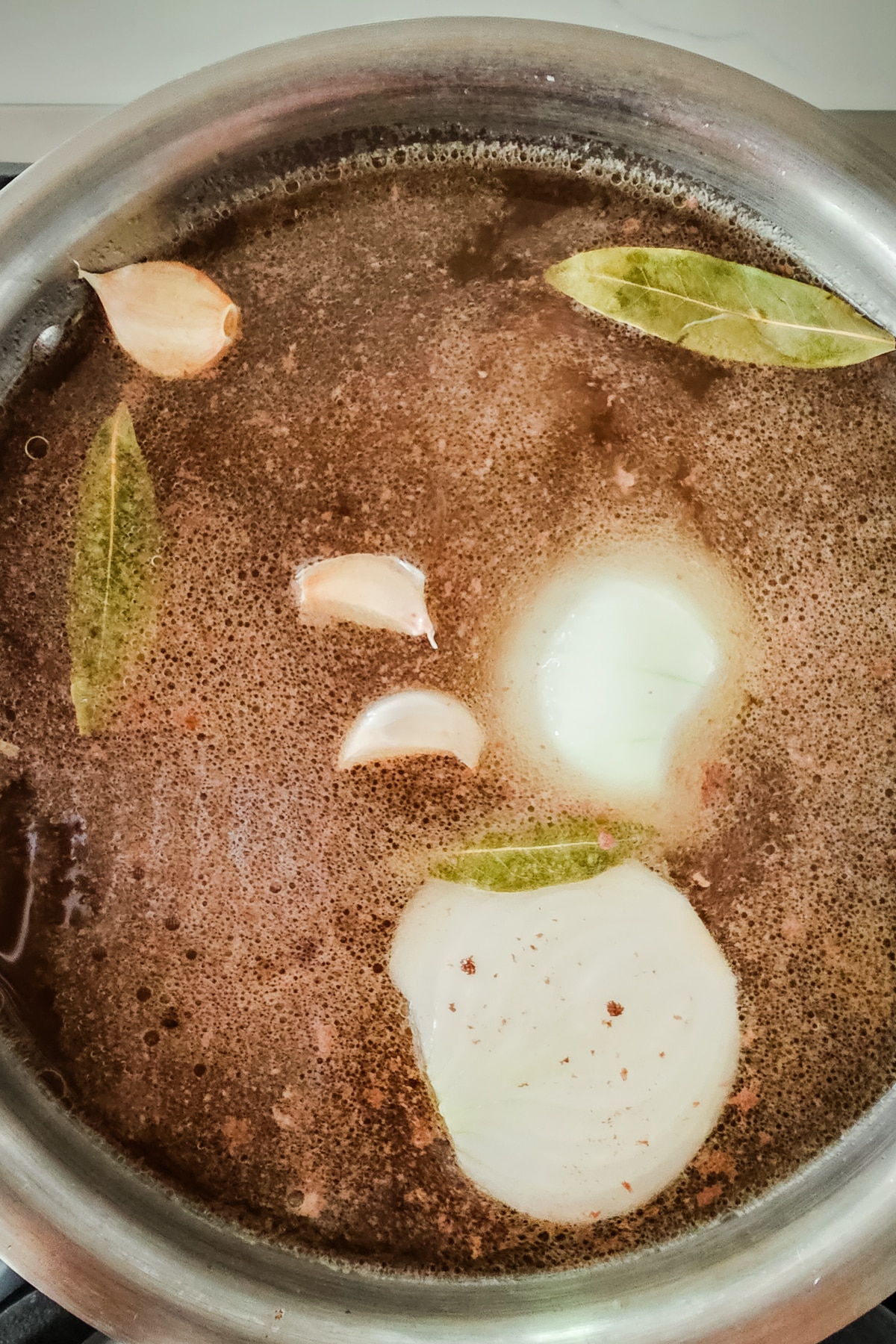 beef broth is cooked in a large pot with onions and bay leaves.
