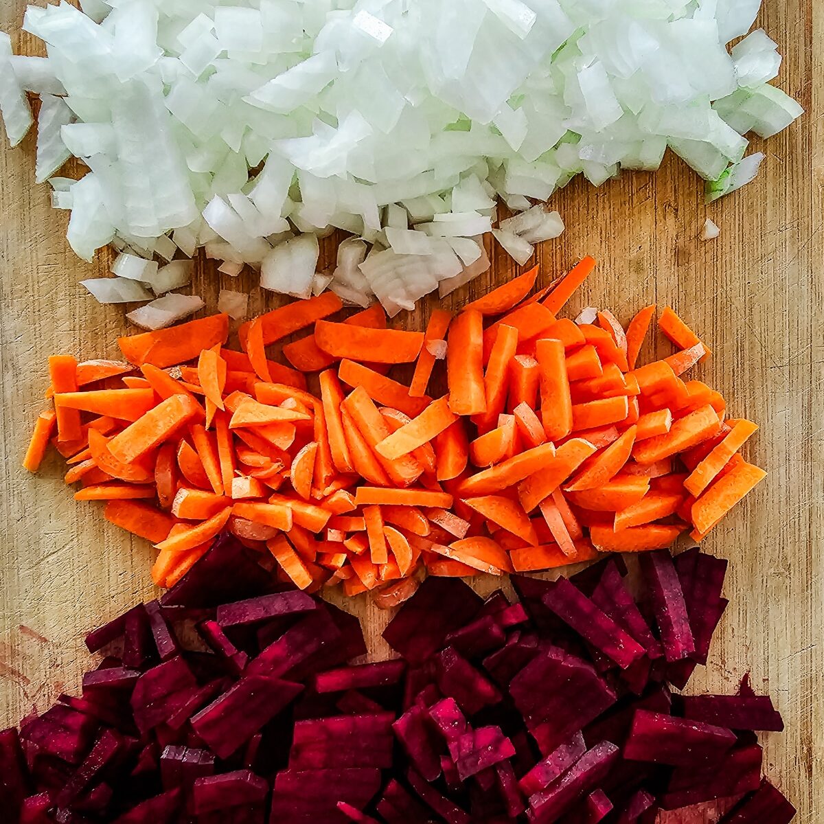 diced onions, cut carrots, beet root, and minced garlic on a wooden cutting board.