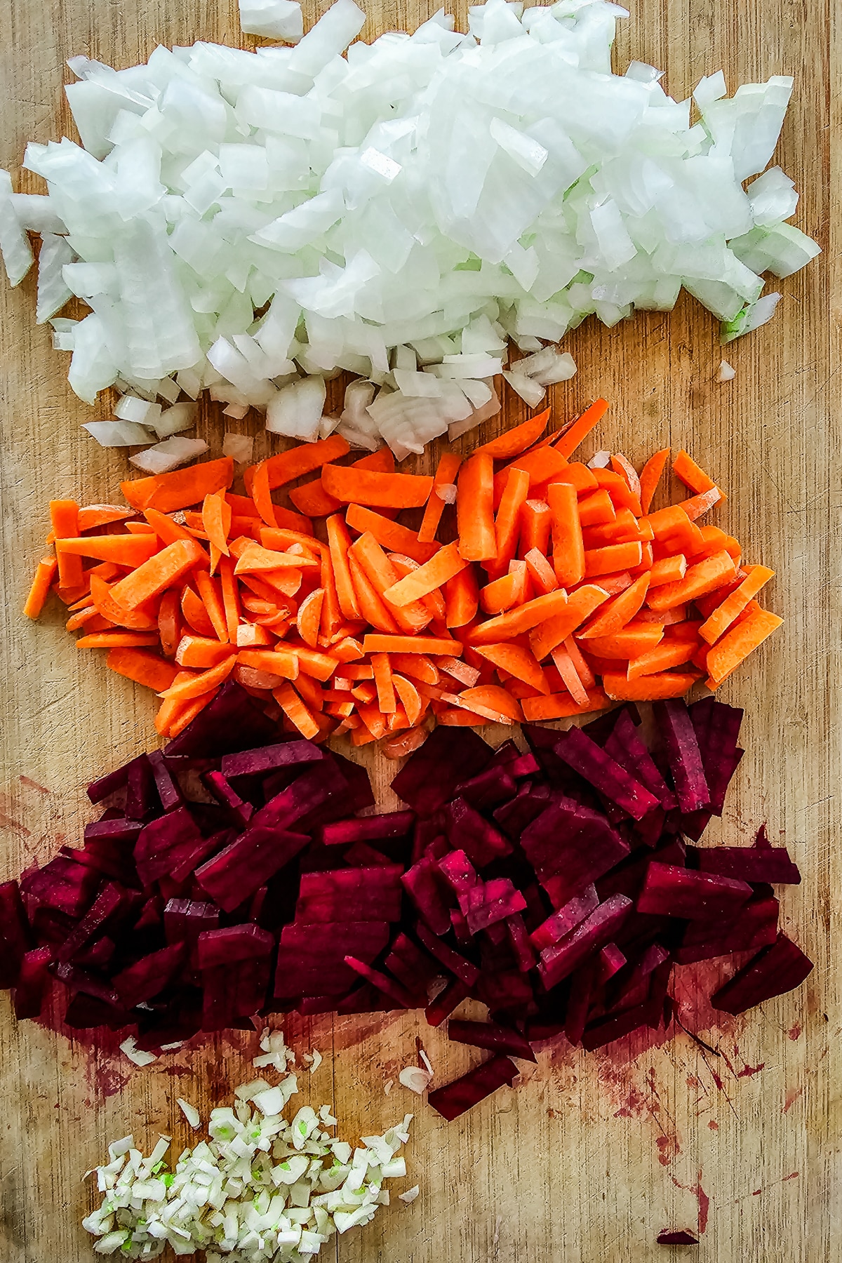diced onions, cut carrots, beet root, and minced garlic on a wooden cutting board.