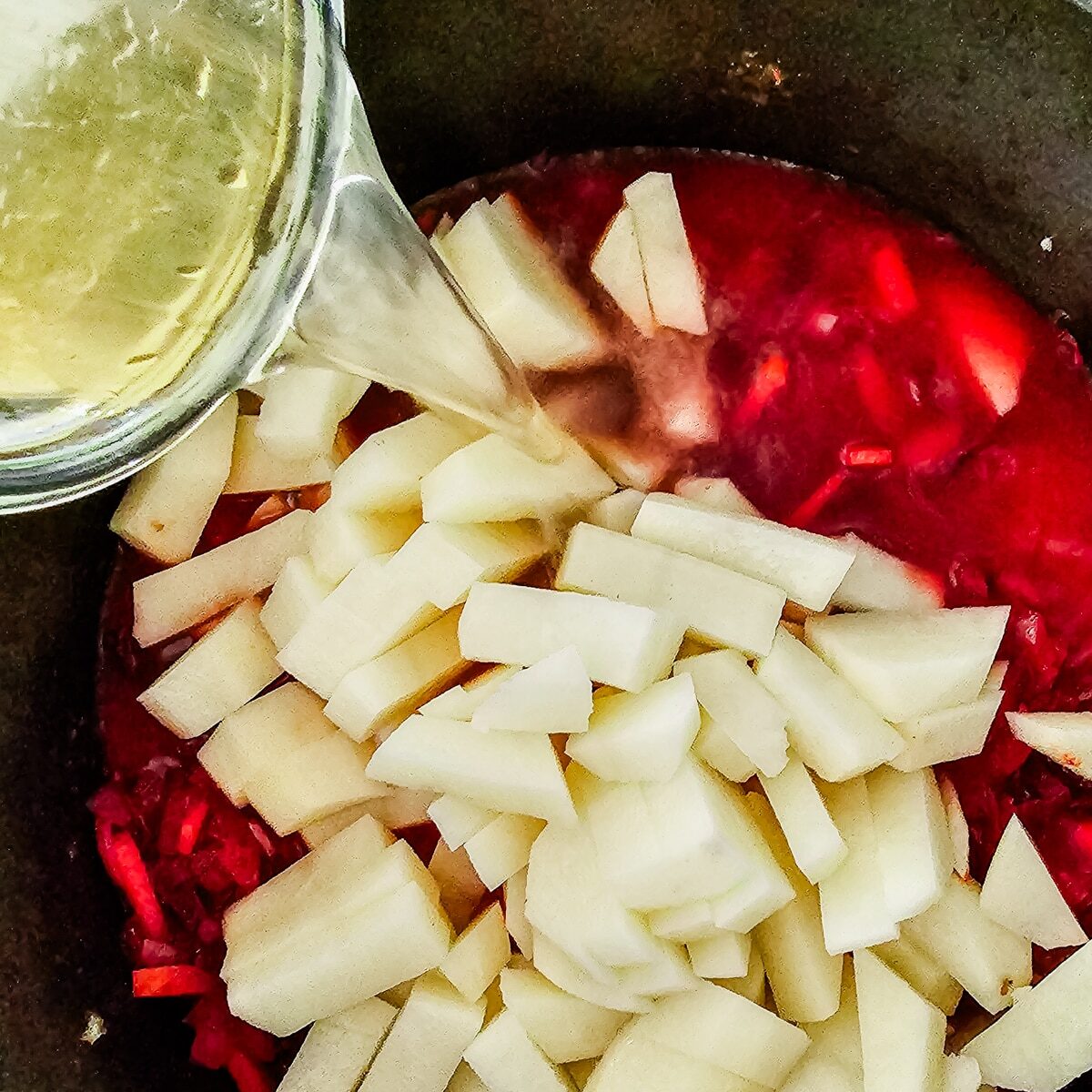 diced potatoes and broth being poured into a pot of beet soup.