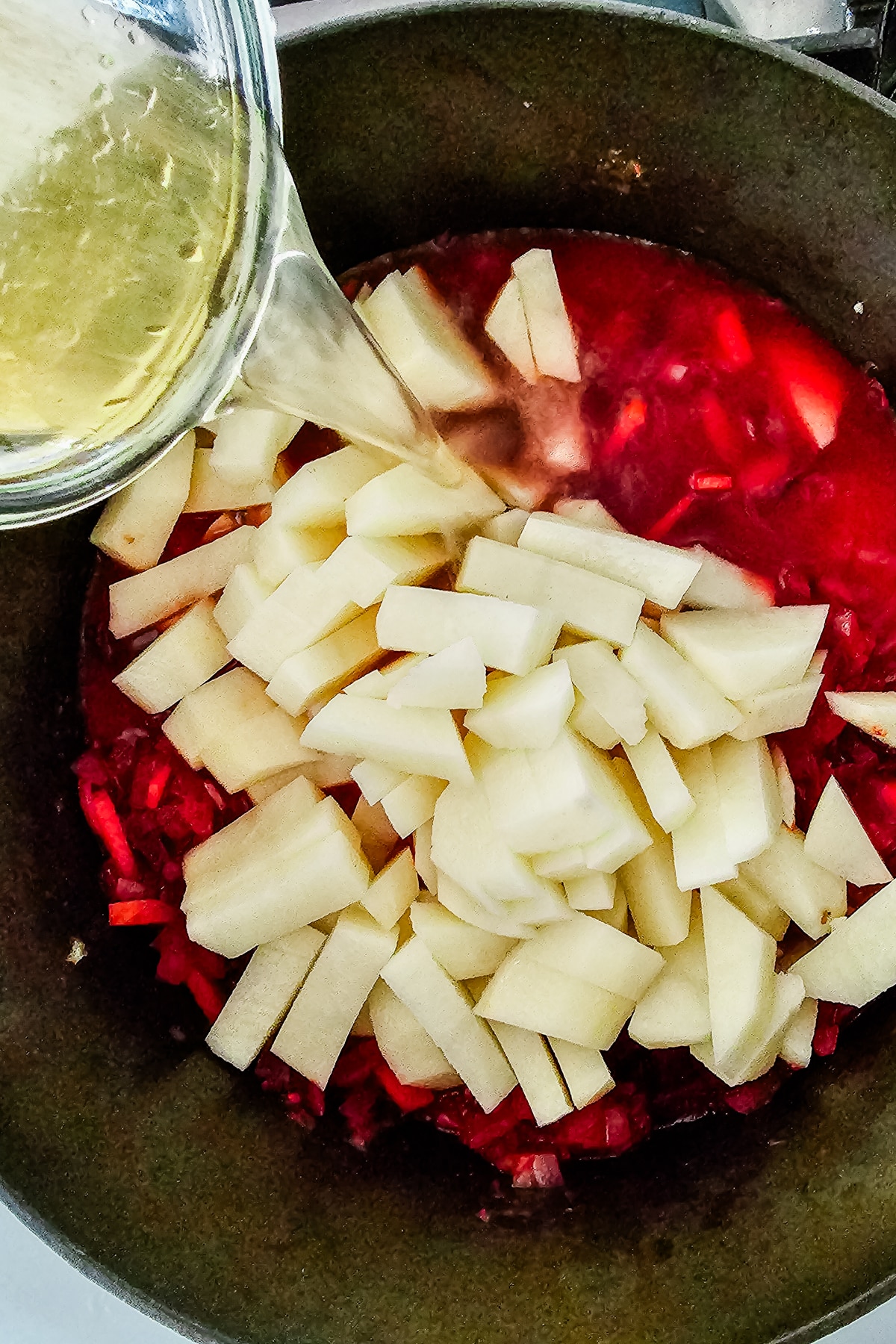 diced potatoes and broth being poured into a pot of beet soup.