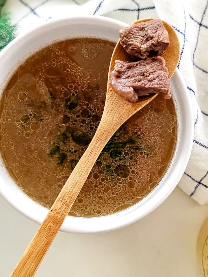 meat stock in a white bowl with wooden spoon gathering meat.