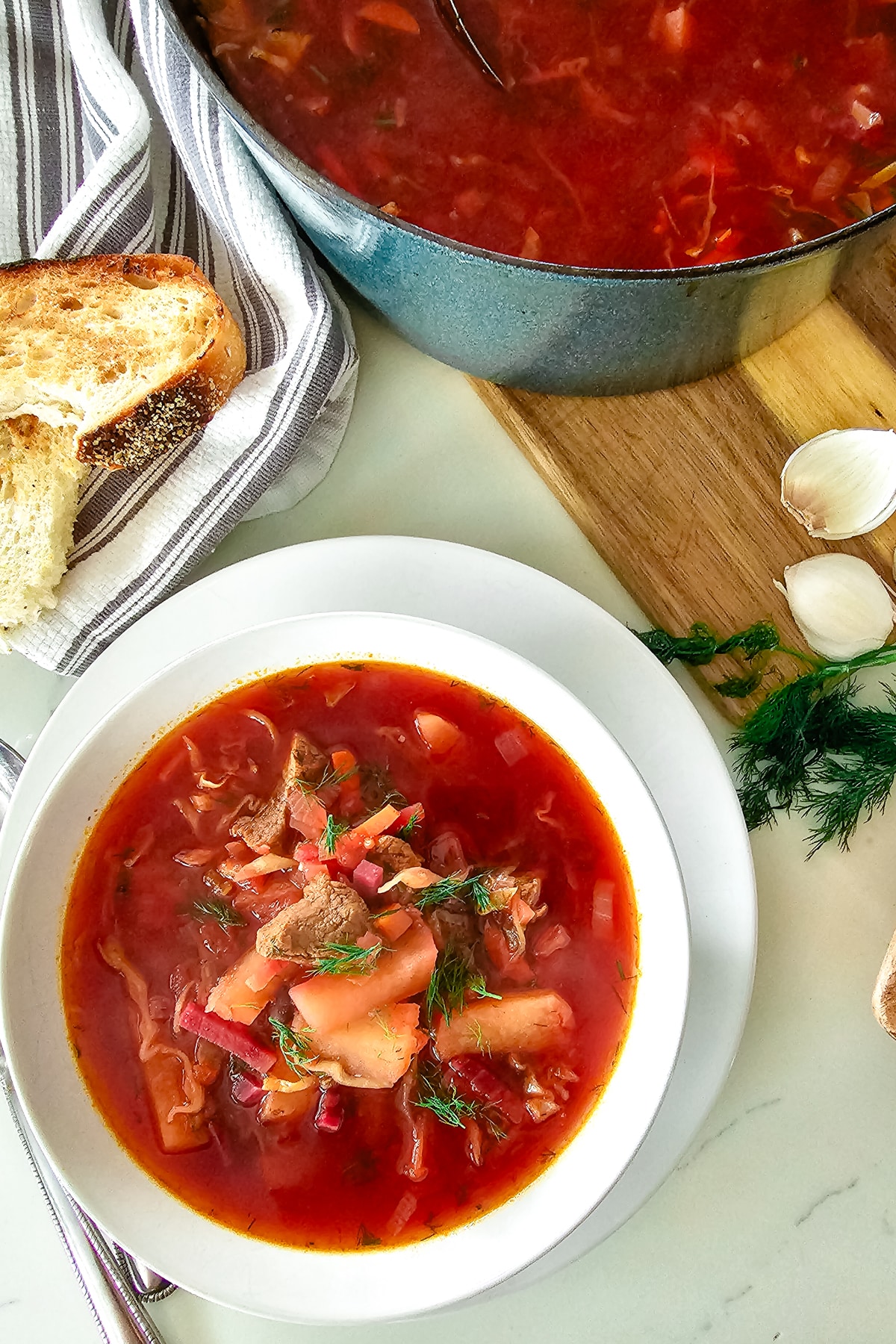 meat borsch in a white bowl with a pot of beet soup to the side.