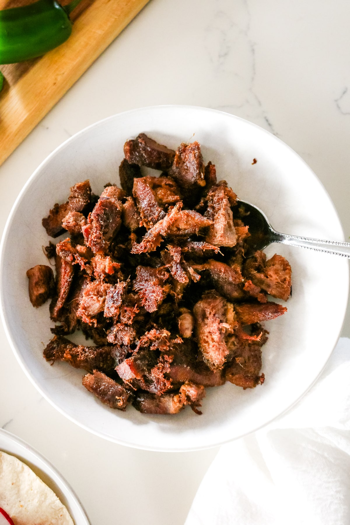 Beef tongue in a white bowl with a spoon sticking out.