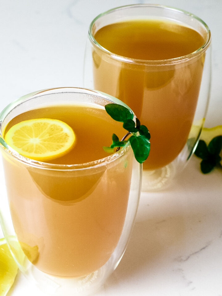 two clear mugs with honey citrus mint tea and lemon slices, lemon wedges, and fresh mint as garnish.