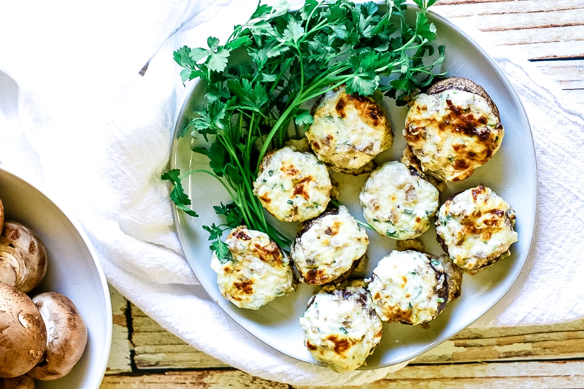 stuffed mushrooms on a white plate with fresh mushrooms to the side.