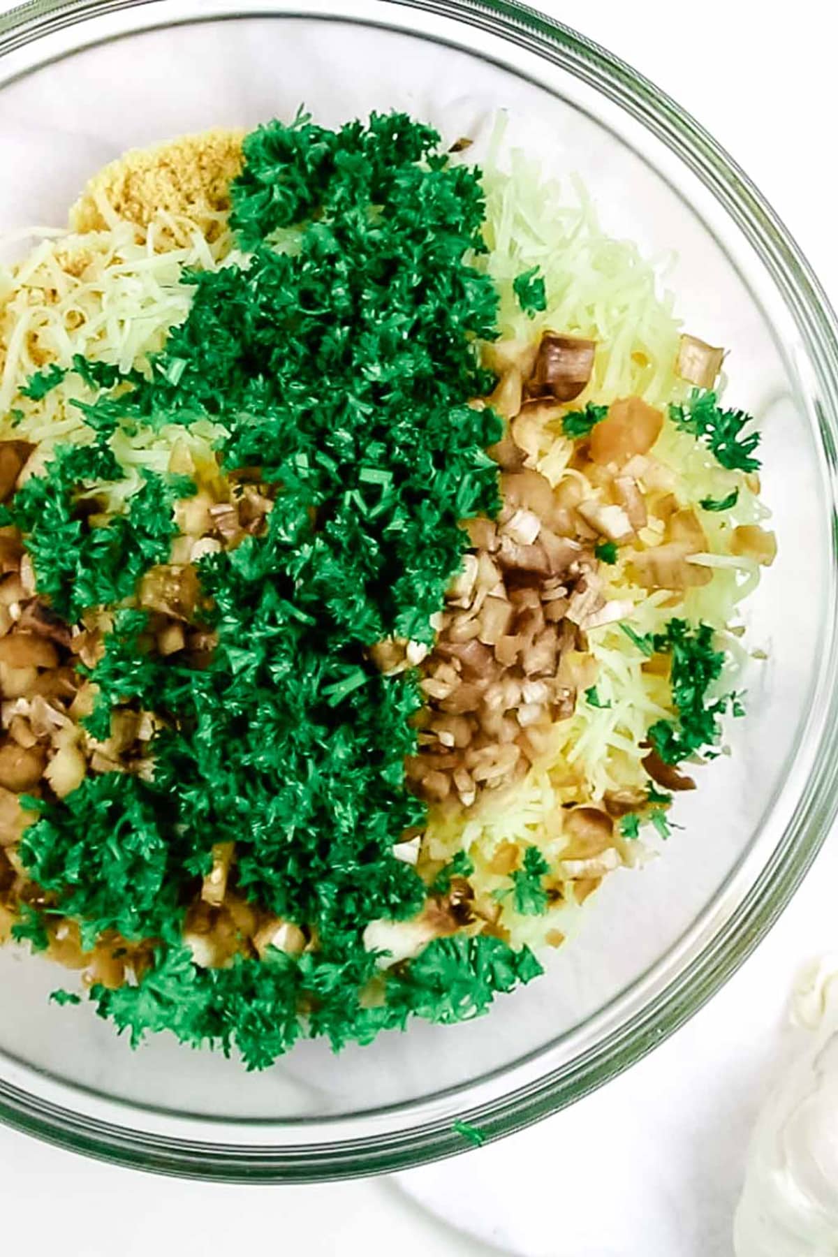 clear glass bowl that holds grated cheese, mushroom stems, and fresh parsley.