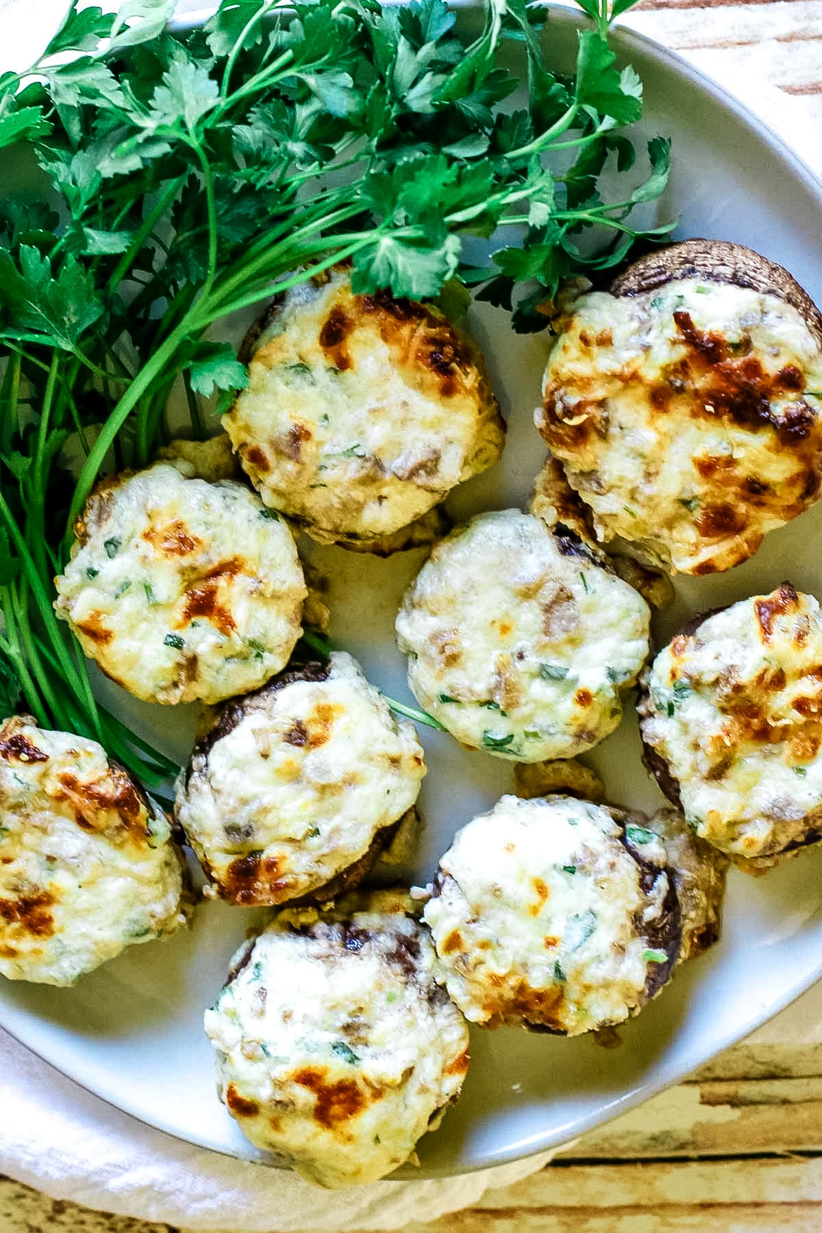 cheese stuffed mushrooms on a white plate with fresh parsley to the side.