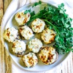 stuffed mushrooms on a white plate with green parsley to the side.