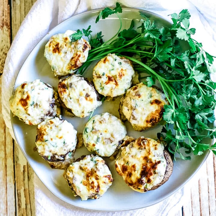 stuffed mushrooms on a white plate with green parsley to the side.