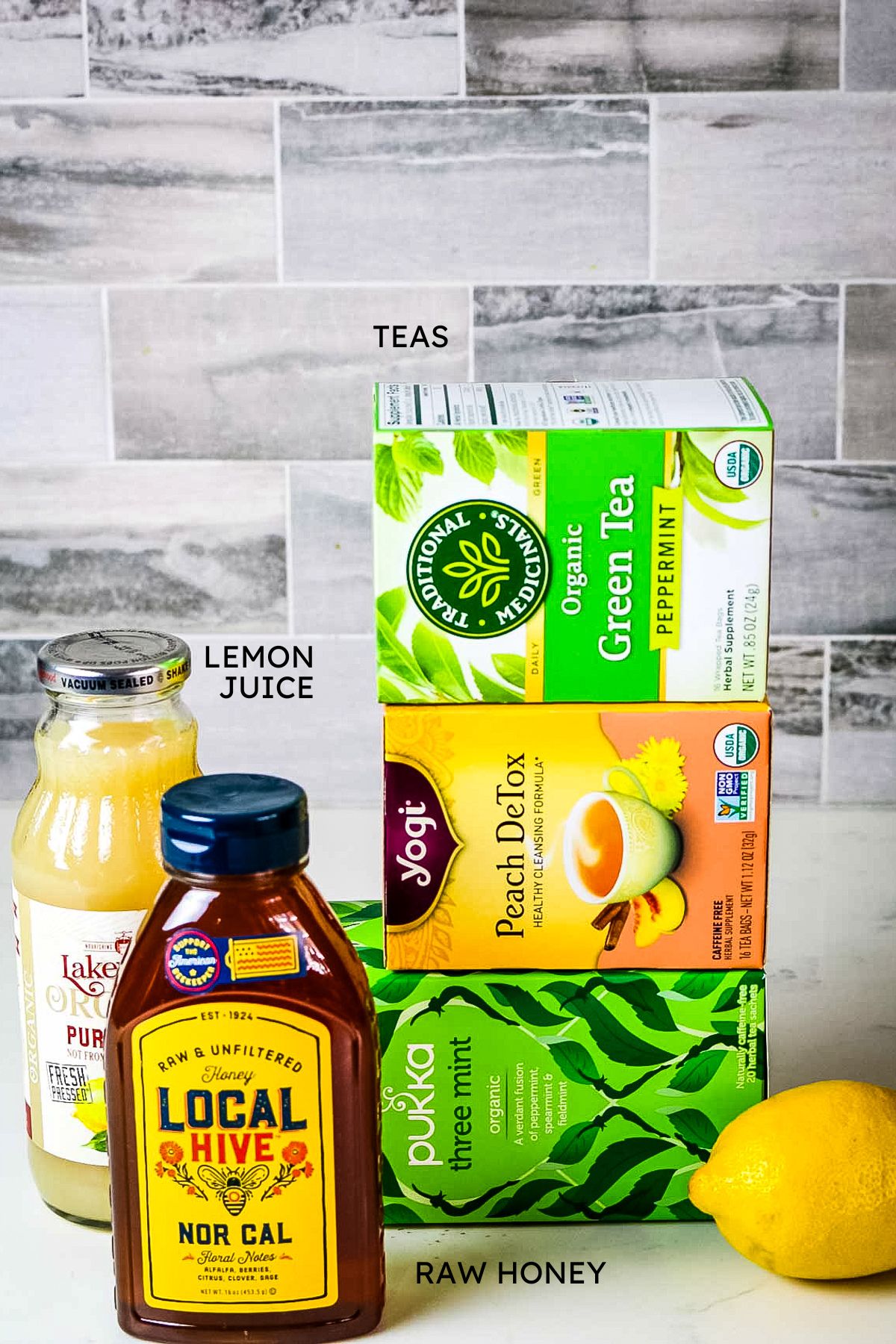 stack of three different tea boxes, fresh lemon, lemon juice in bottle and local and raw honey bottle.