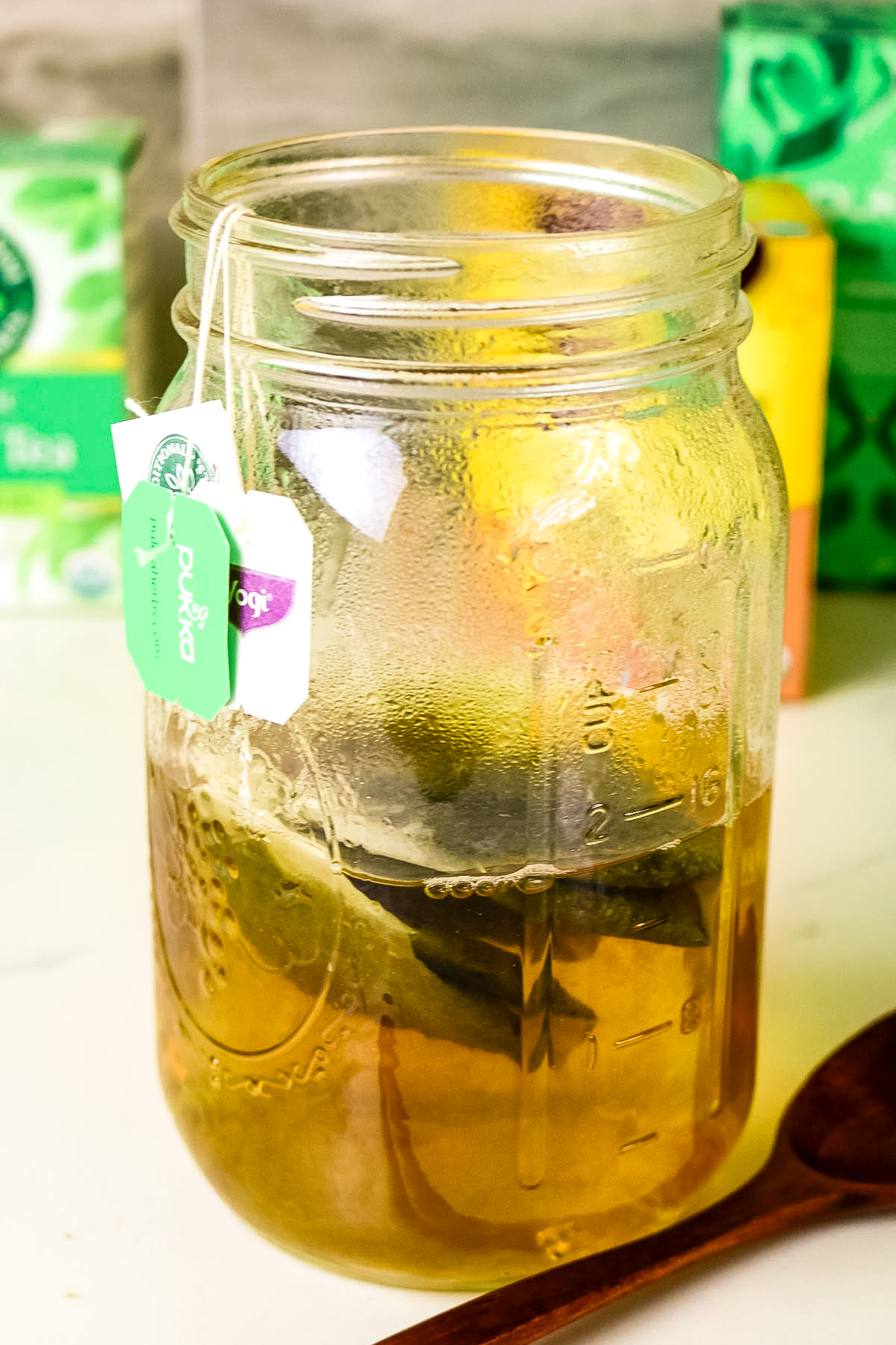three tea bags steeped in hot water in a mason jar with wooden spoon to the side.