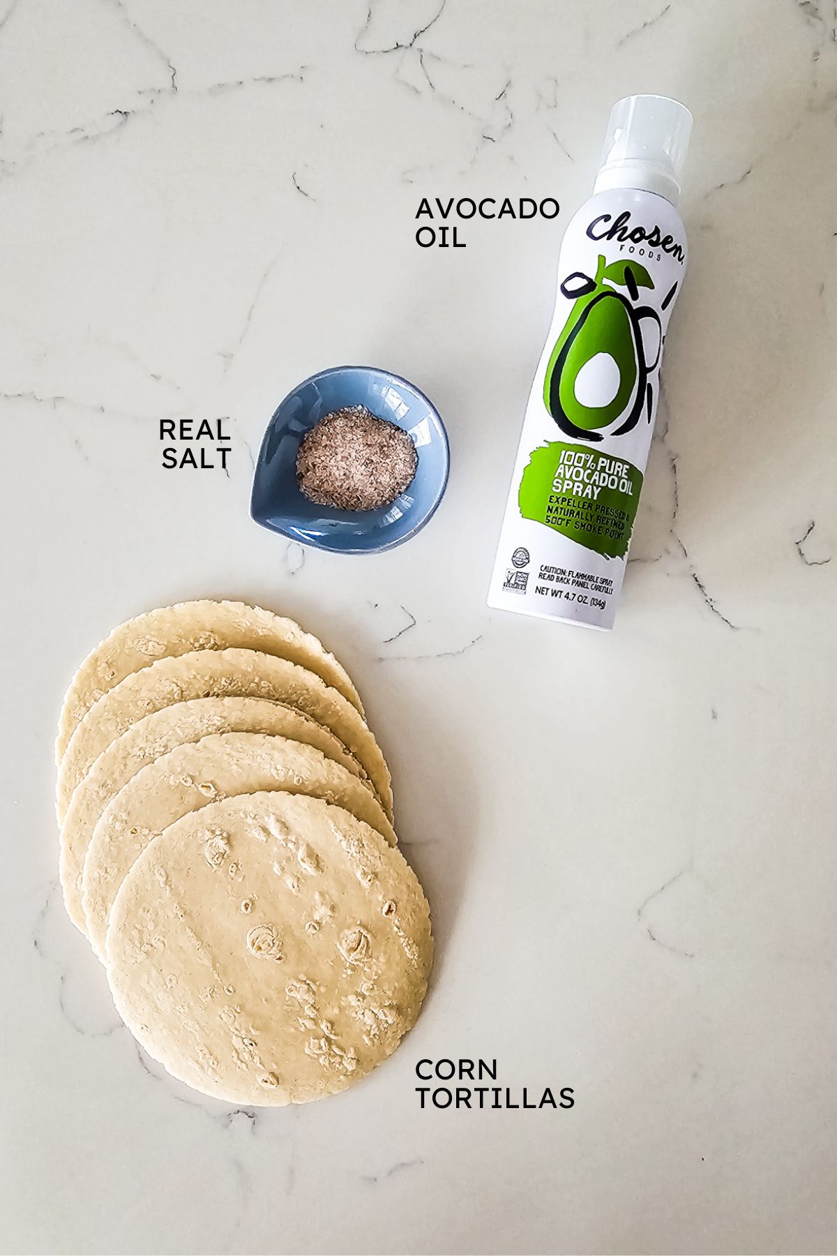 Ingredients to make tortilla chips on a counter top including avocado oil, salt, and tortillas.