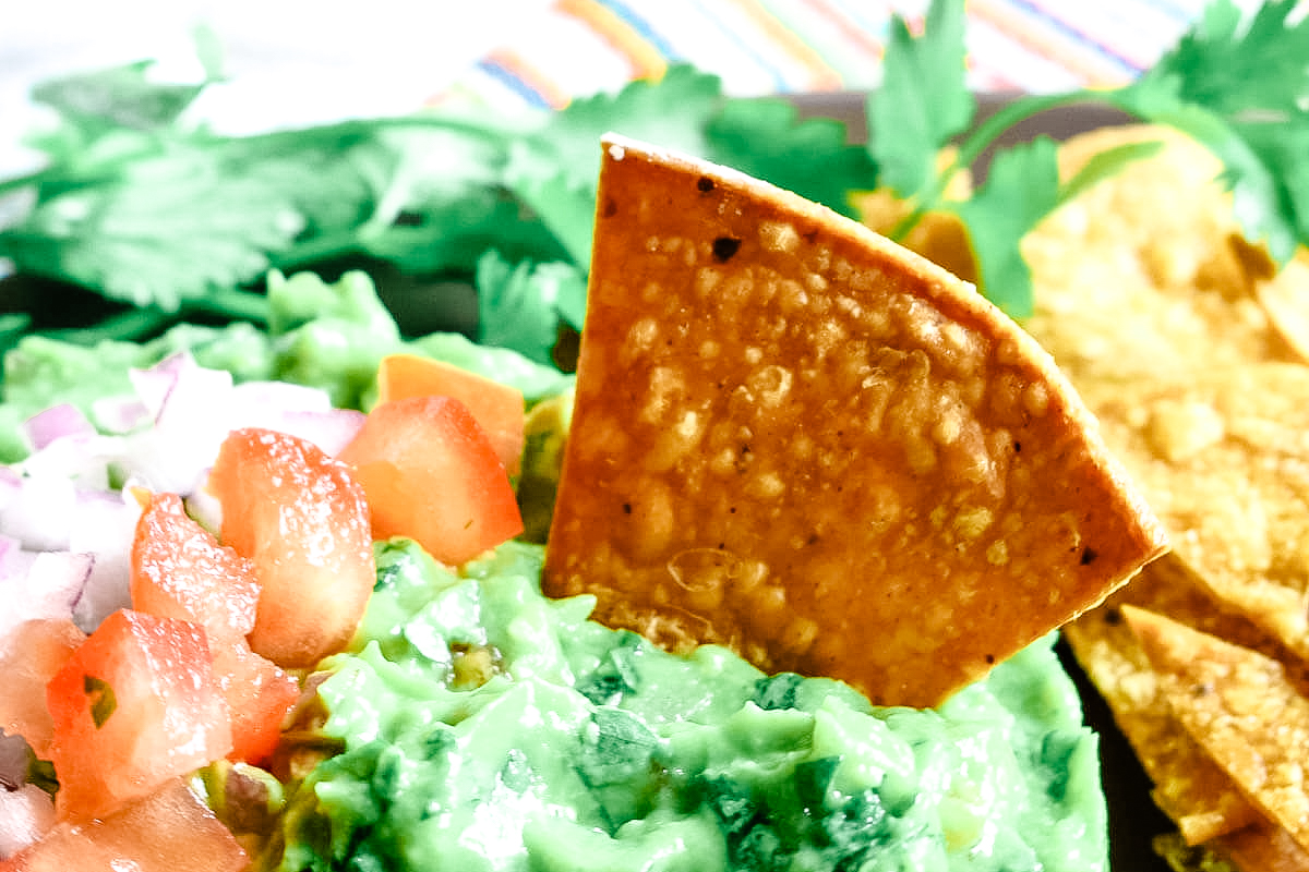 Tortilla chip sticking out of a pile of colorful guacamole.