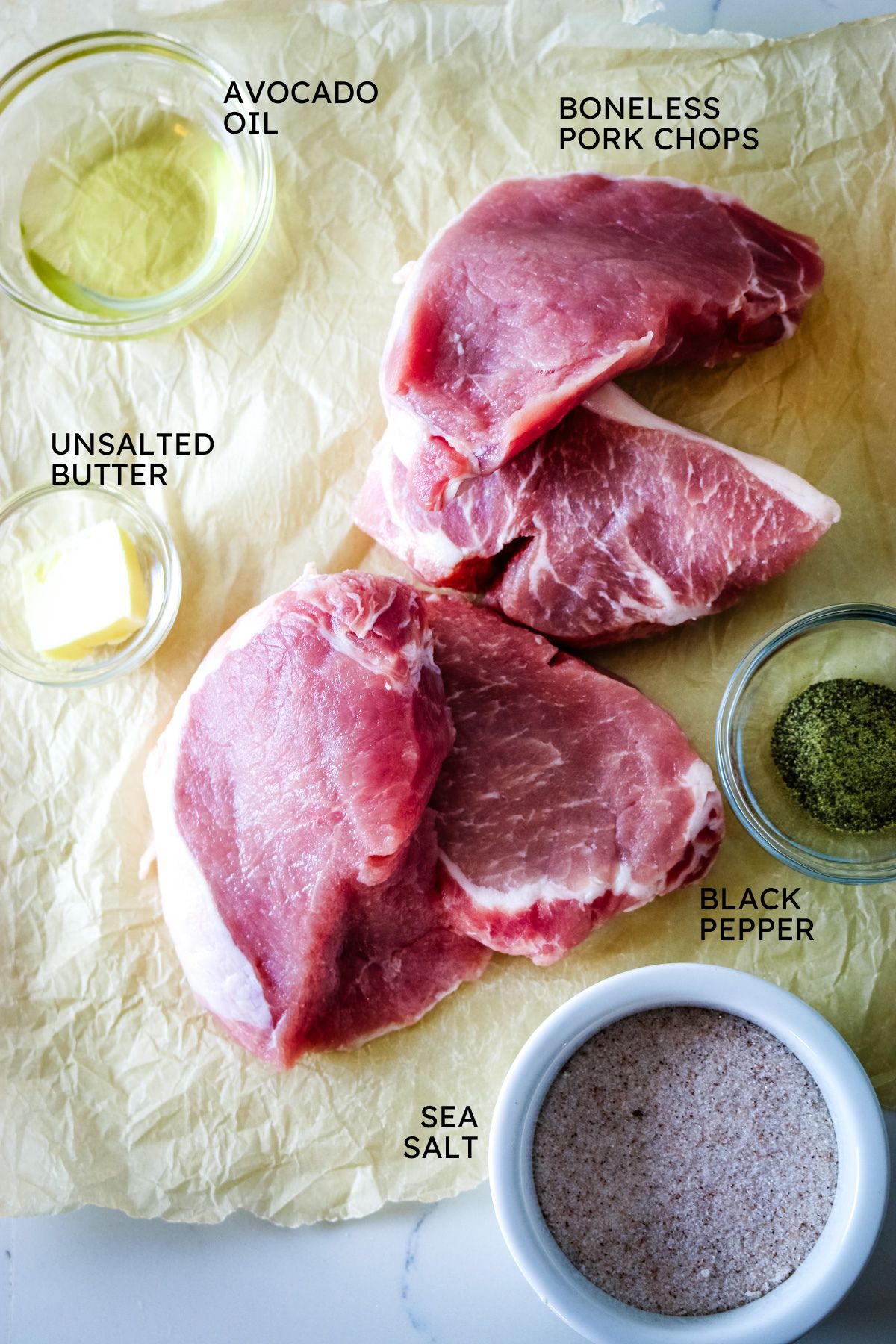 ingredients spread out on parchment paper, pork chops, oil, butter, salt and pepper.