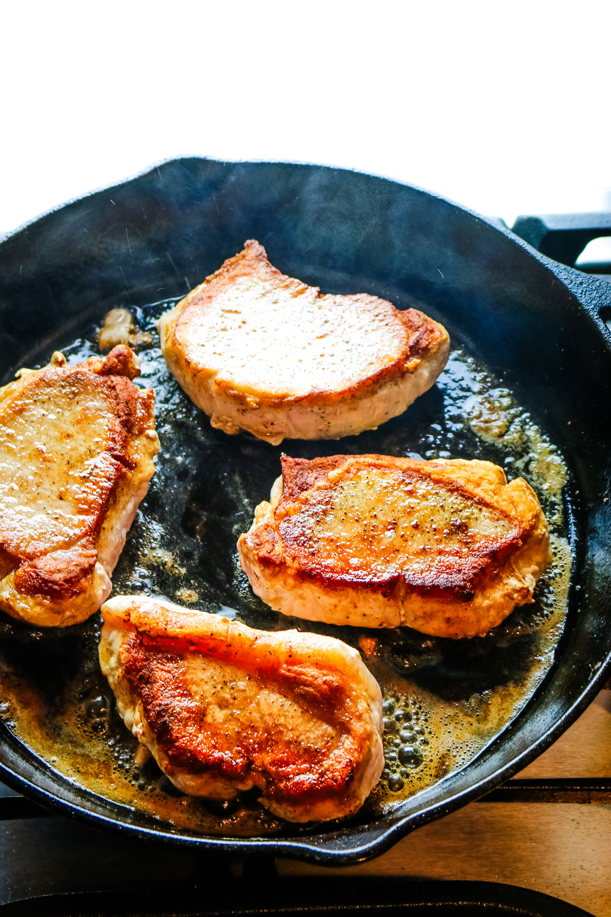 four pork chops searing on a butter with butter.