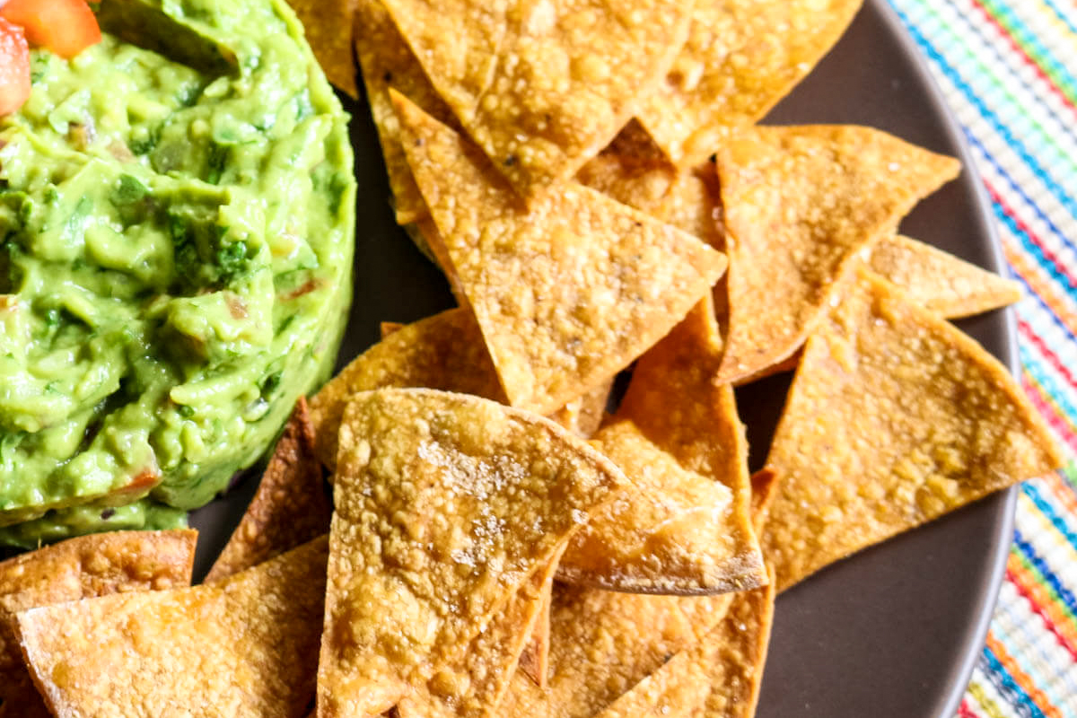 Tortilla chips with salt on the right side of a guacamole mountain.
