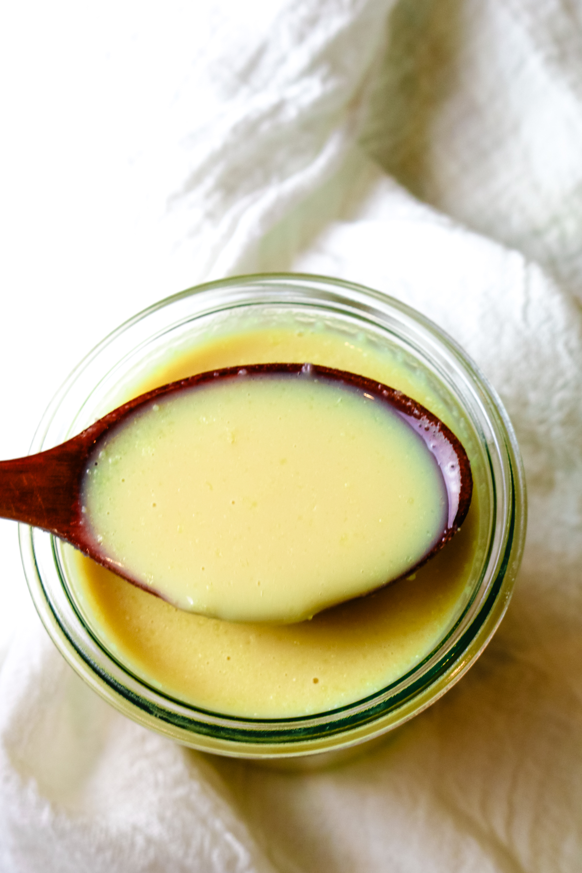 a glass jar filled with condensed milk and a wooden spoon with some condensed milk on it over the jar.