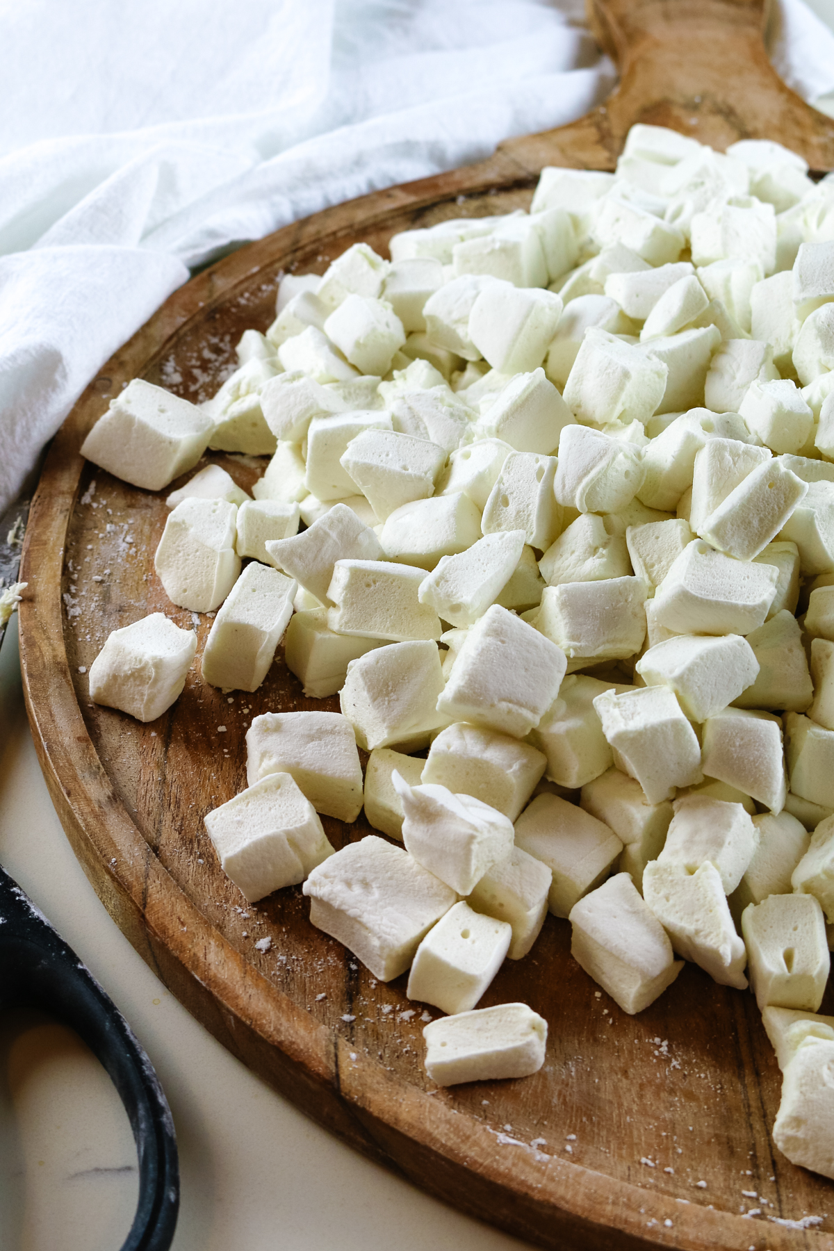 marshmallows cut into small pieces on a wooden cutting board with a pair of kitchen shears to the side.