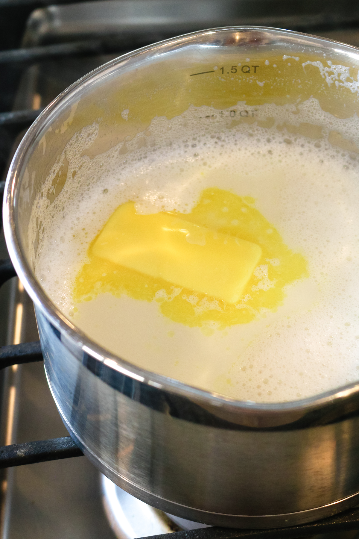 whisked milk inside of a metal pan with a slice of butter inside of it.