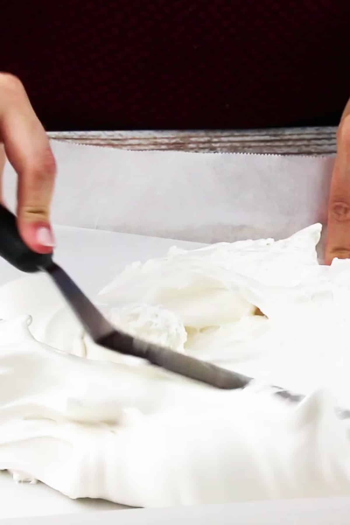 marshmallow fluff being spread out on a sheet pan lined with parchment paper.
