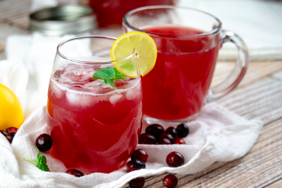 cranberry juice in a glass and a mug with fresh cranberries scattered around it.