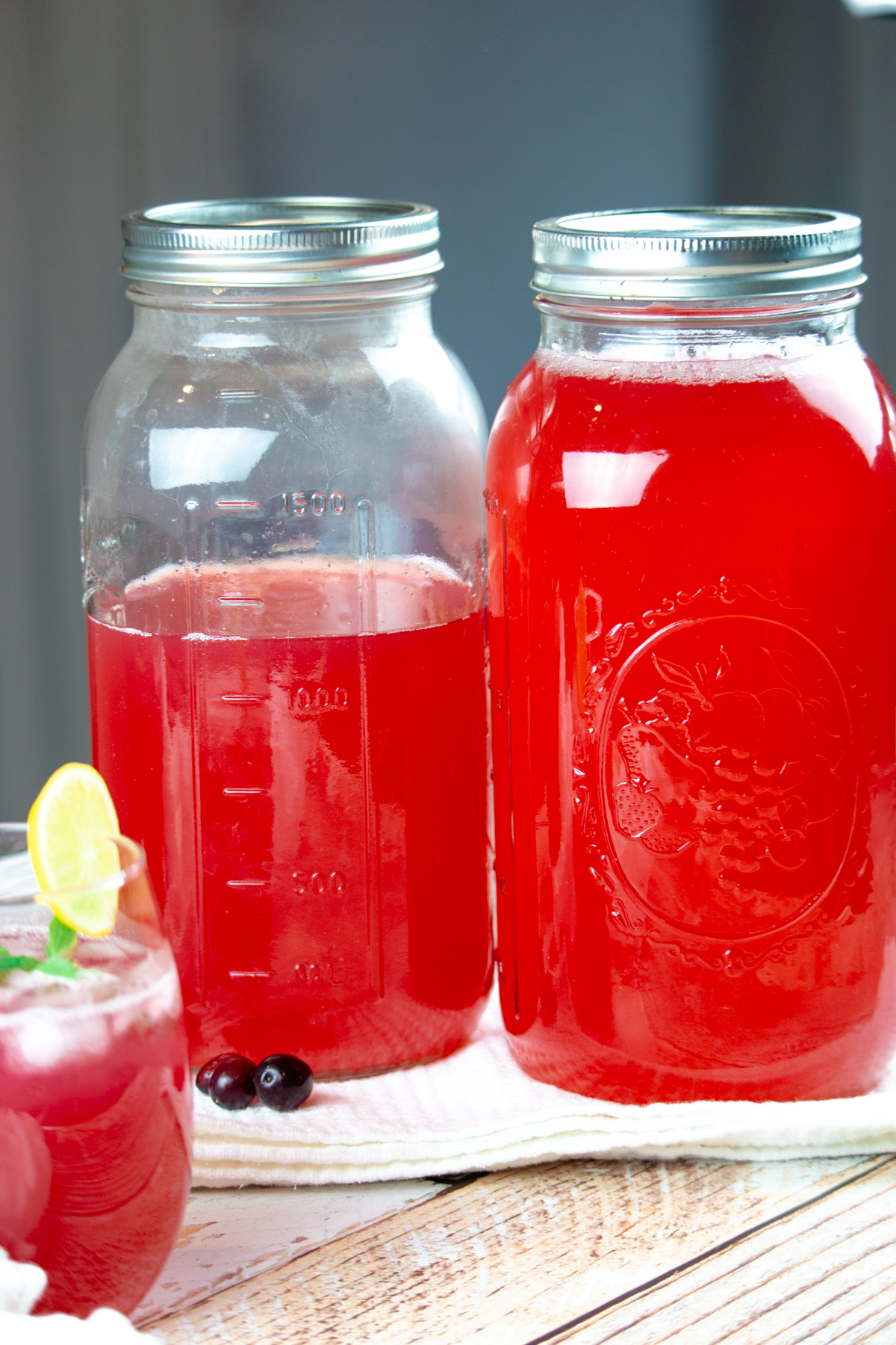 cranberry juice in half-gallon mason jars with fresh cranberries in front.