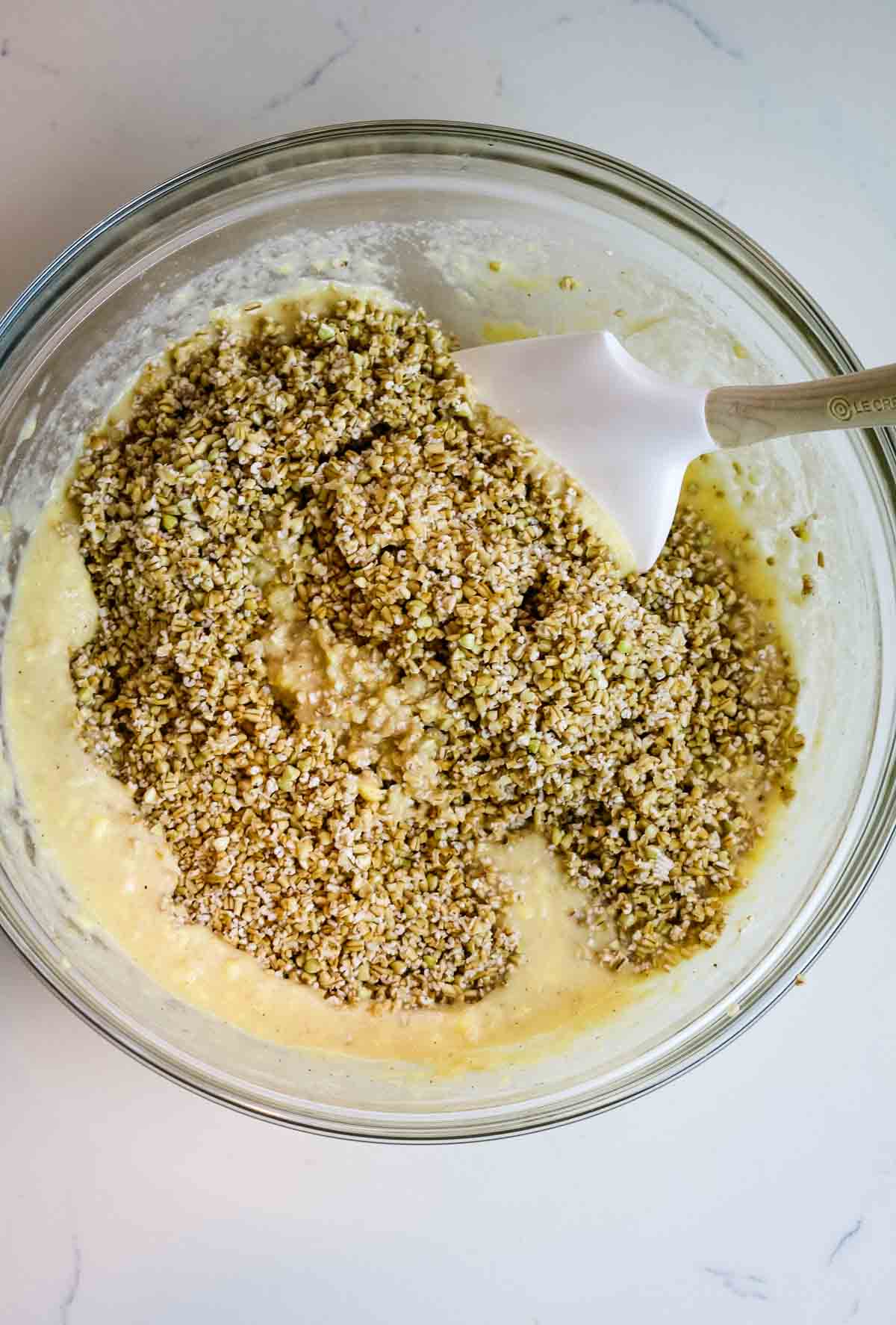 plastic spatula in a bowl with oats and other ingredients on white counter
