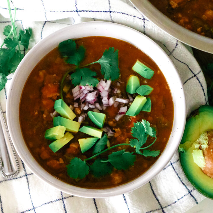 healthy pumpkin turkey chili in a white bowl with fresh cilantro and red onions as garnish.