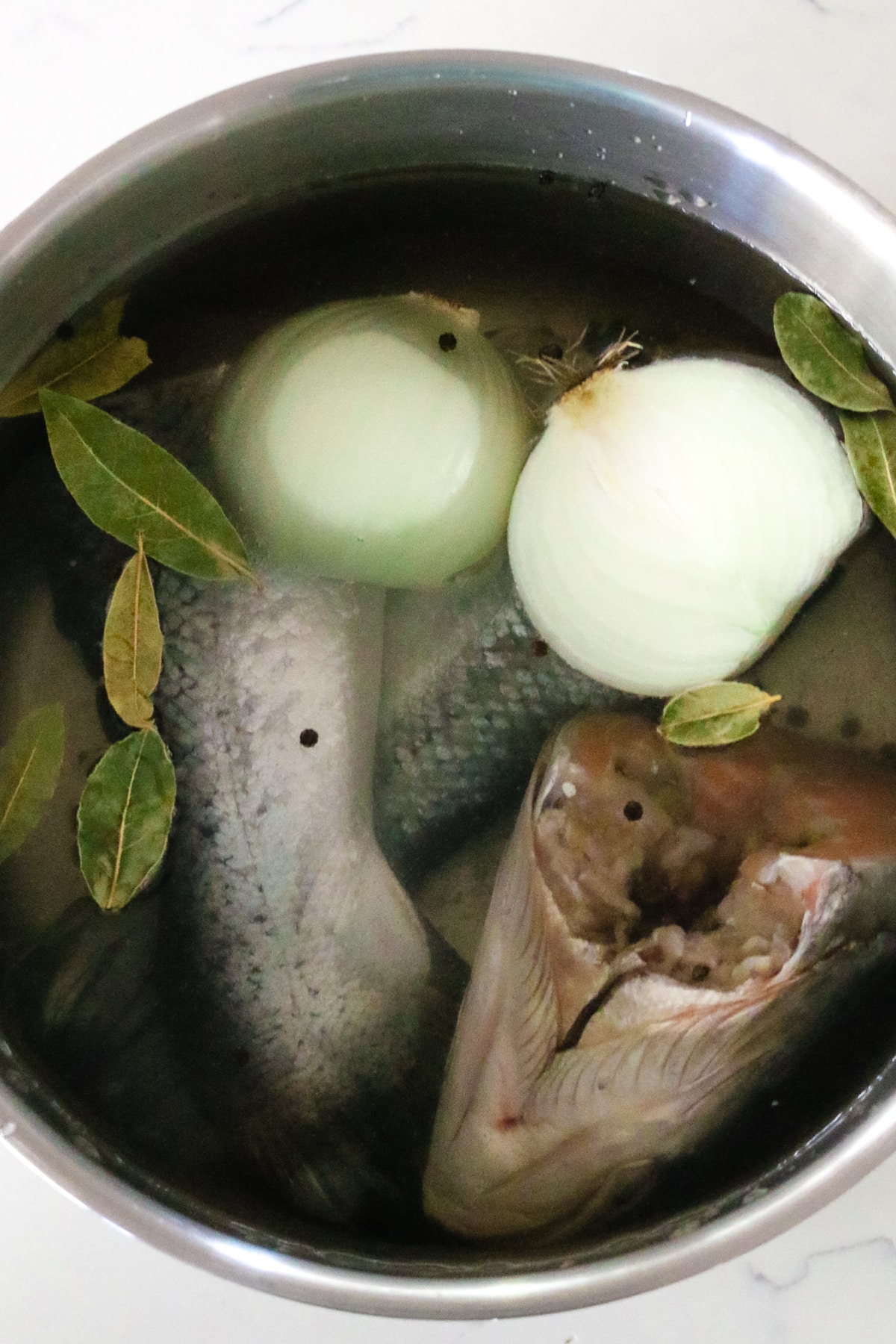uncleaned fish in water with onions and bay leaves inside of steal bowl